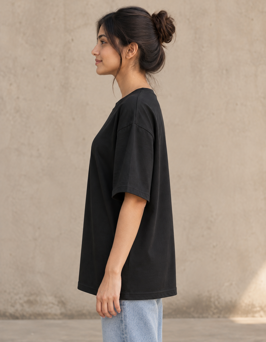 Styling illustration · left side profile · Black Qikink UC22 oversized T-shirt on an Indian adult model. Shared view of the same unprinted garment surface; not a produced-sample photograph.