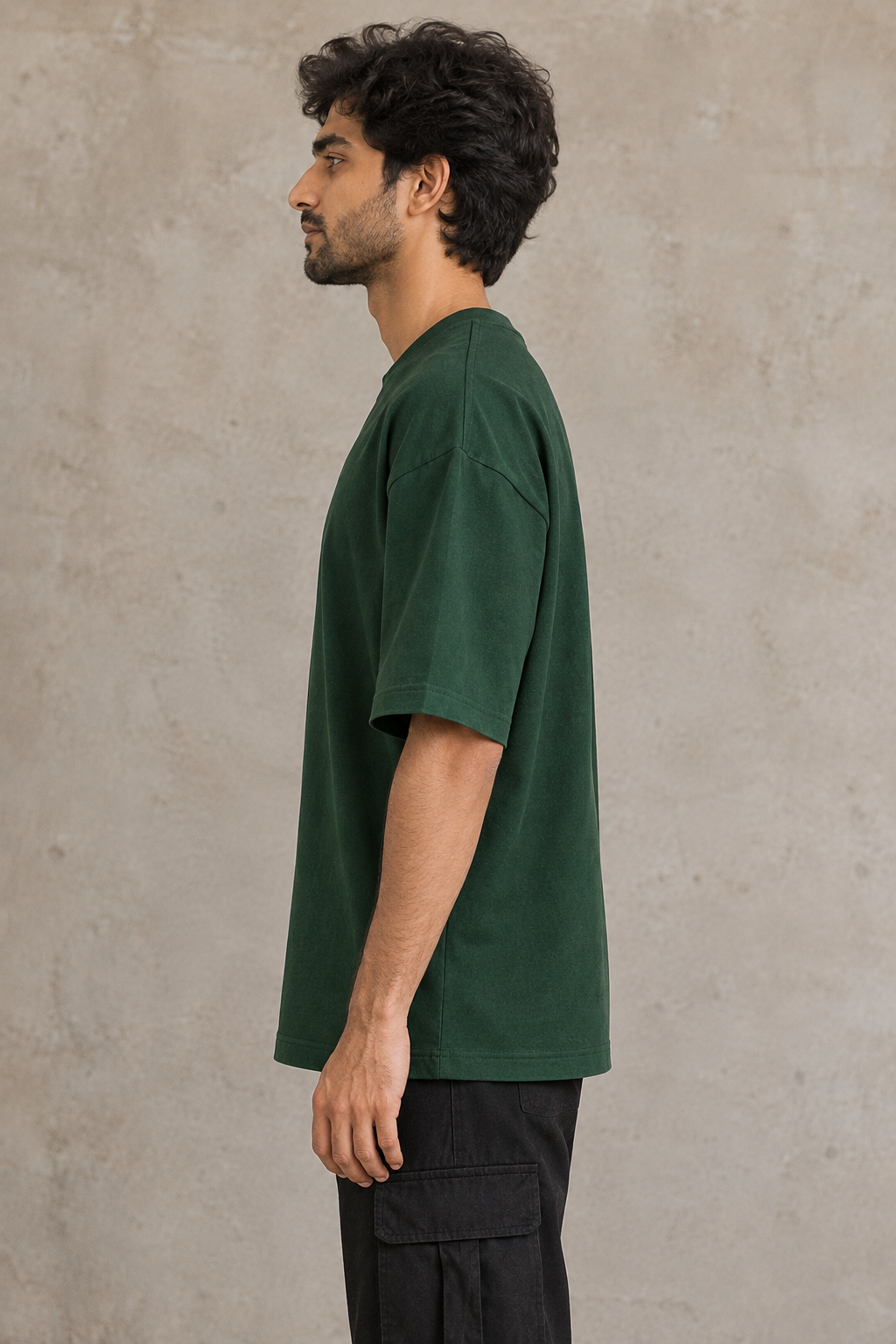Styling illustration · left side profile · Bottle Green Qikink UC22 oversized T-shirt on an Indian adult model. Shared view of the same unprinted garment surface; not a produced-sample photograph.